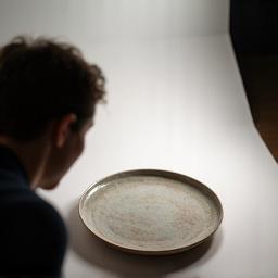 Ang isang photographer ay kumukuha ng larawan ng isang ceramic plate sa isang propesyonal na studio, kumakatawan sa execution ng photoshoot.